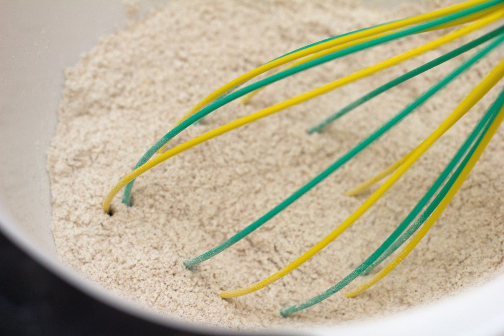 Whole wheat flour and baking powder in mixing bowl with whisk.