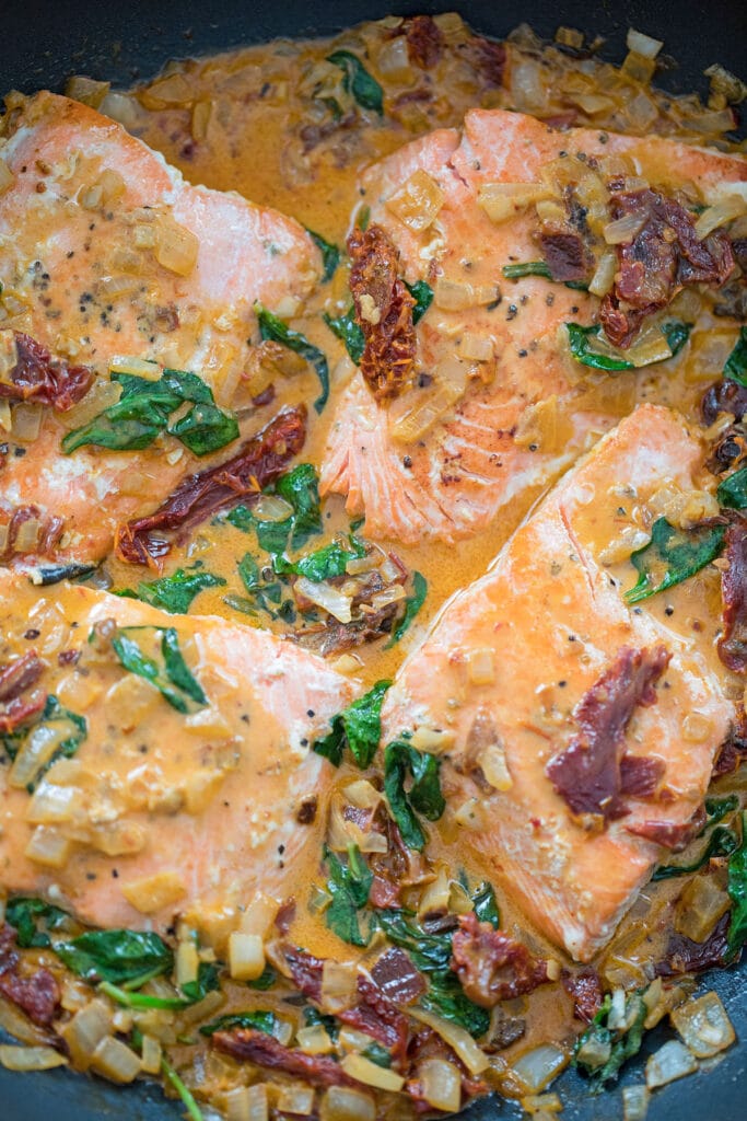 Overhead view of skillet with chipotle salmon in creamy sauce with spinach and sun-dried tomatoes.