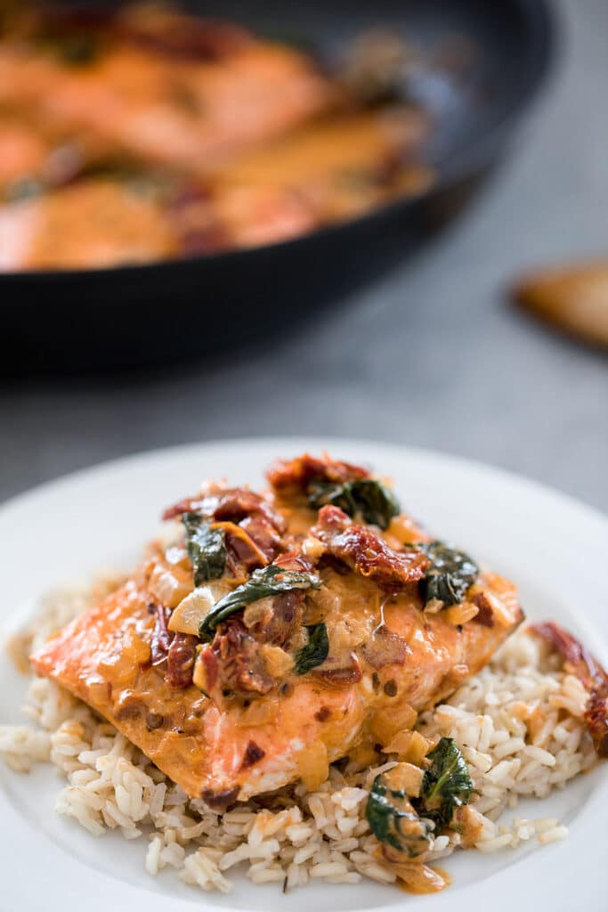 Piece of salmon with creamy chipotle sauce over a bed of rice on a plate with skillet in background.
