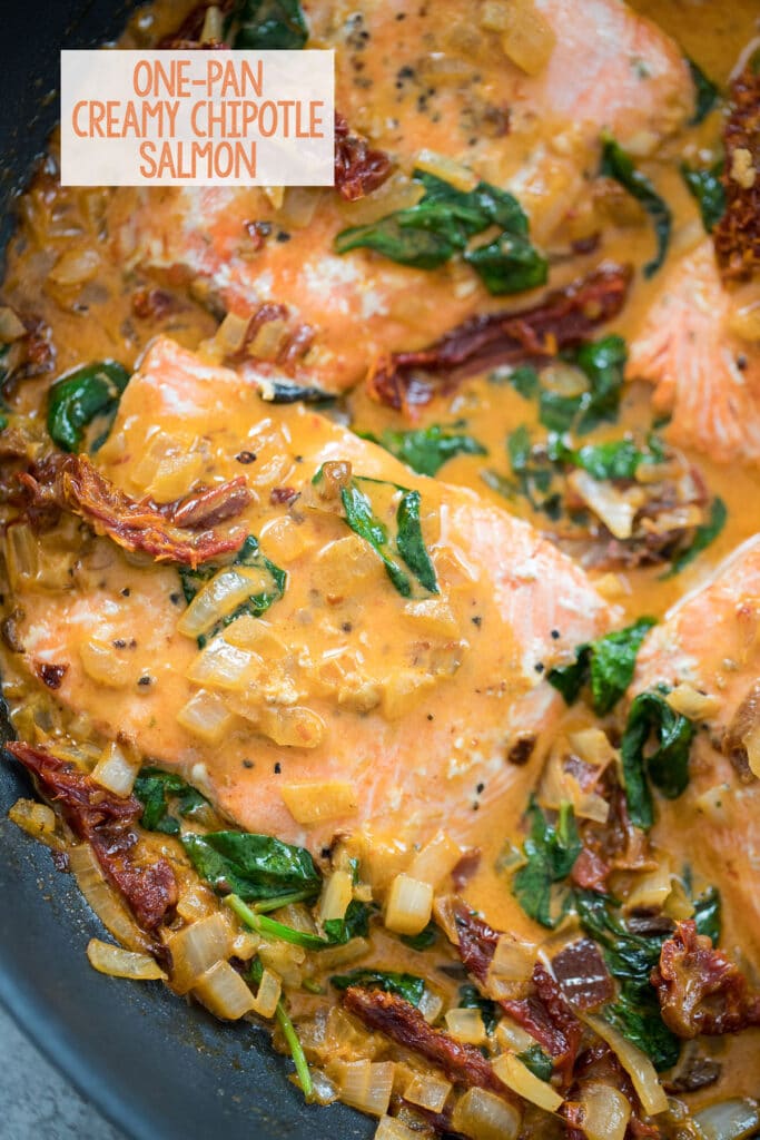 Overhead closeup view of chipotle salmon in skillet with sun-dried tomatoes, spinach, and creamy sauce with recipe title at top.