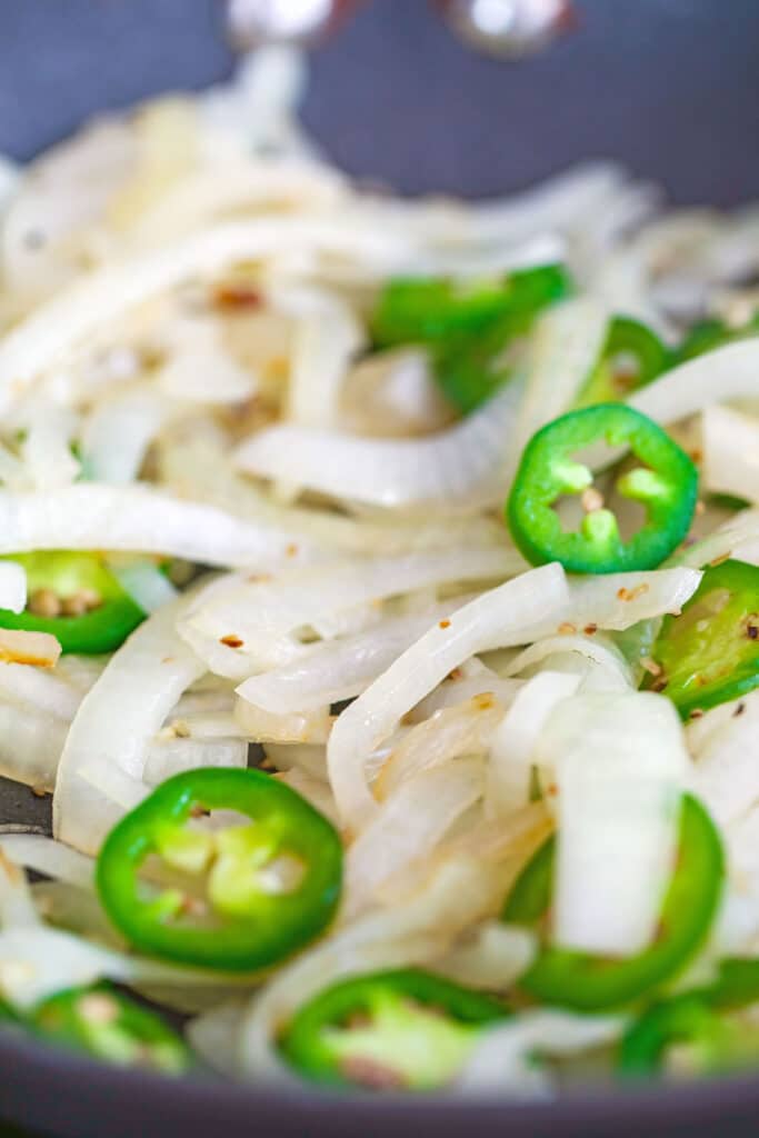 Onions and sliced jalapeño peppers cooking in pan