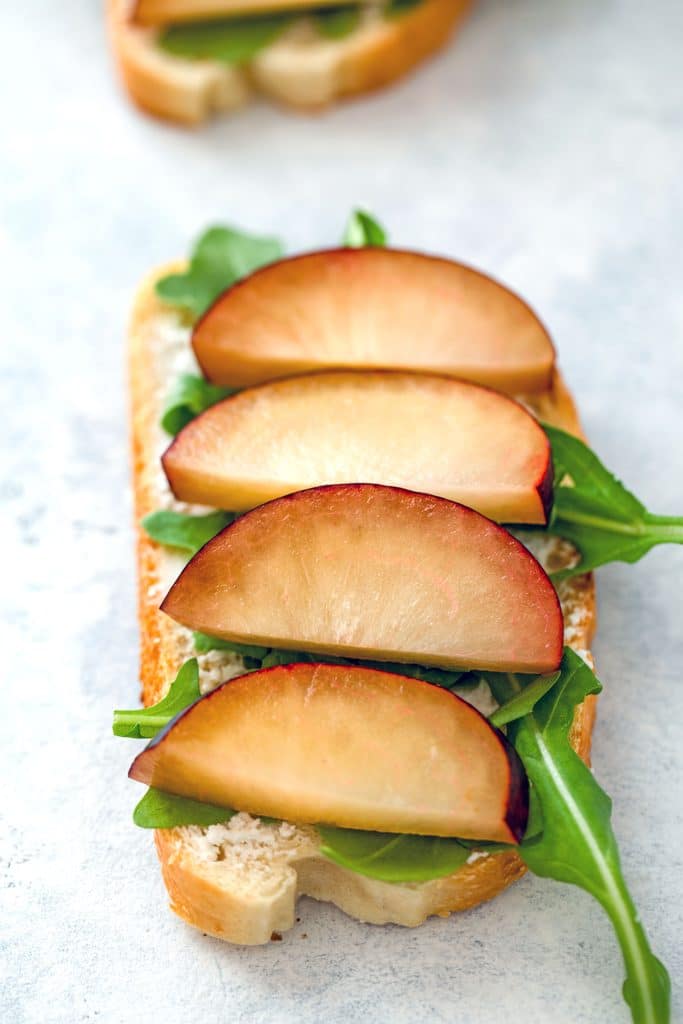 Overhead view of open-faced sandwich spread with goat cheese and topped with arugula and sliced plums