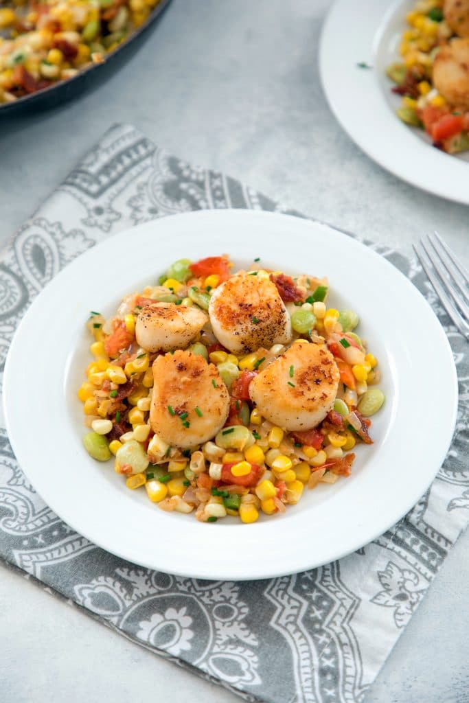 Overhead view of white bowl filled with corn and bacon succotash and topped with seared sea scallops