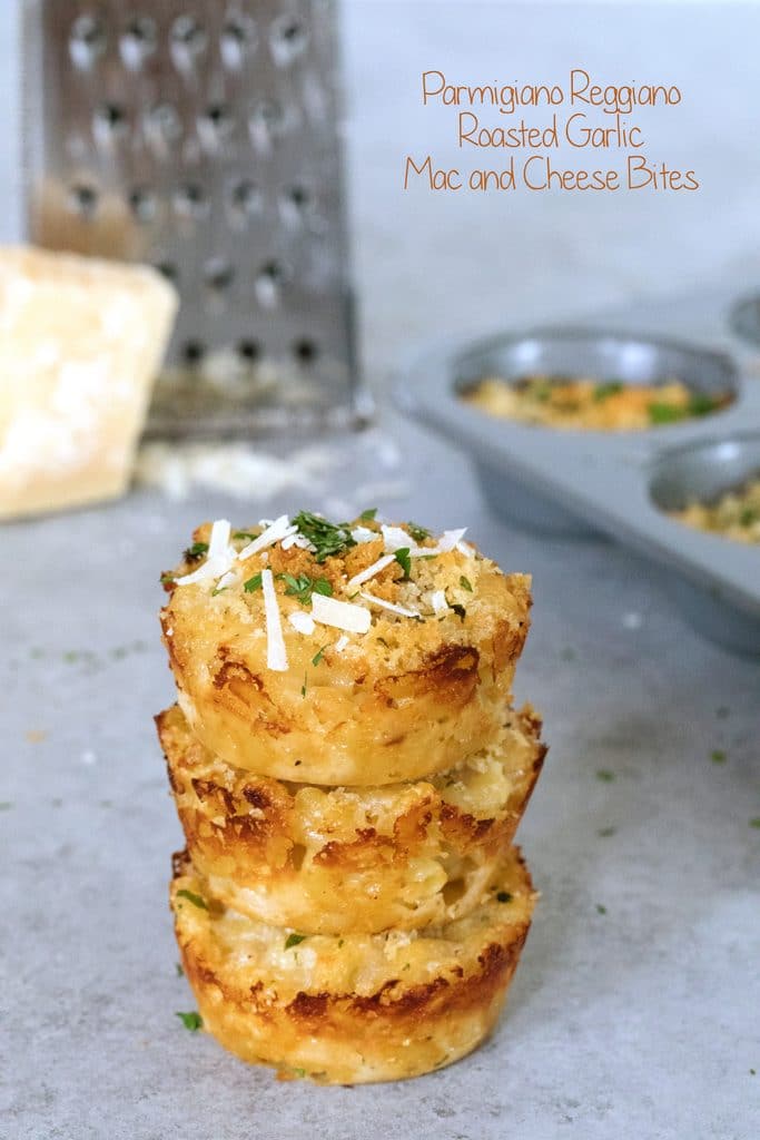 Head-on view of a stack of three mac and cheese bites with block of parmigiano reggiano and grater in background and tin of more mac and cheese bites with recipe title at top