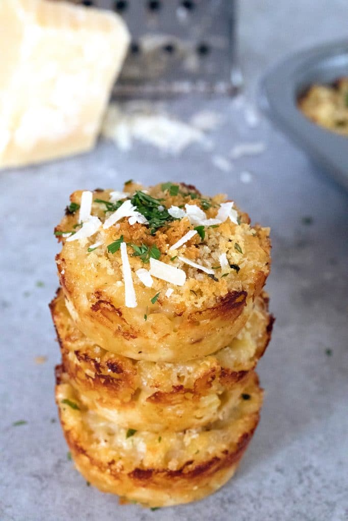 Overhead view of a stack of three mac and cheese bites with block of parmigiano reggiano and grater in background