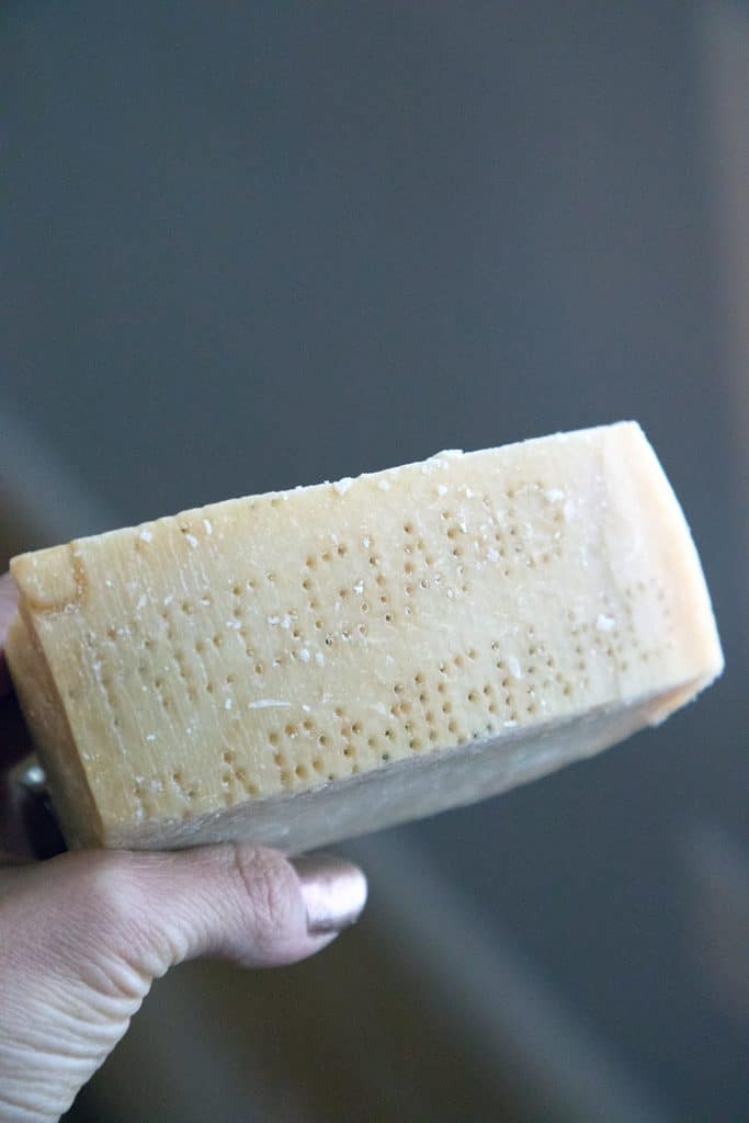 Hand holding up block of cheese to see parmigiano reggiano dot text on rind