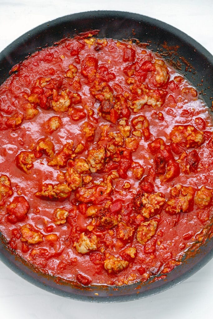 Skillet with crumbled sausage and tomato sauce cooking