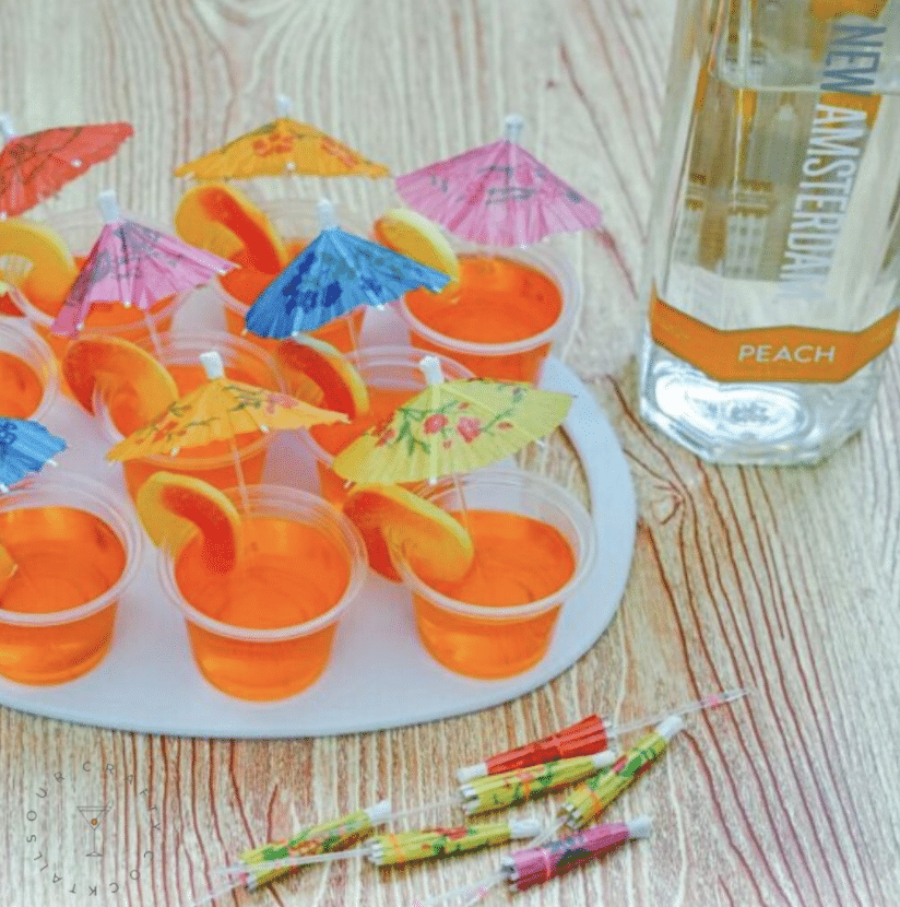 Peach jello shots in little cups with peach ring and paper umbrella garnish