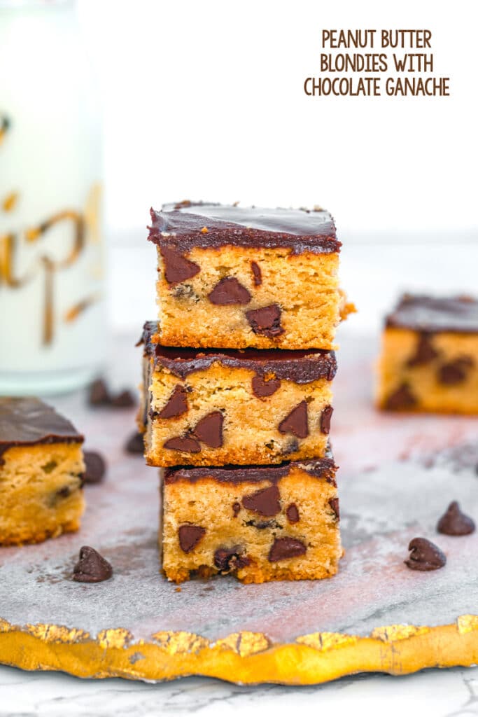 Head-on close-up view of a stack of peanut butter blondies with chocolate ganache and chocolate chips with more blondies and bottle of milk in the background and recipe title at top