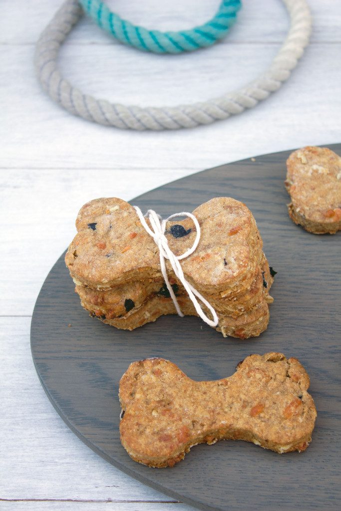 Overhead view of peanut butter cheddar dog bones stacked on a wood platter with a dog leash in the background