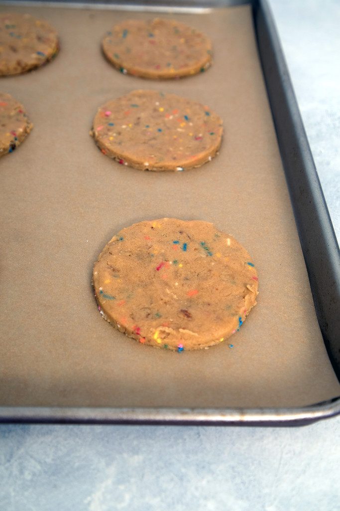 XL peanut butter cookies with sprinkles cut out and set on parchment paper-lined baking sheet