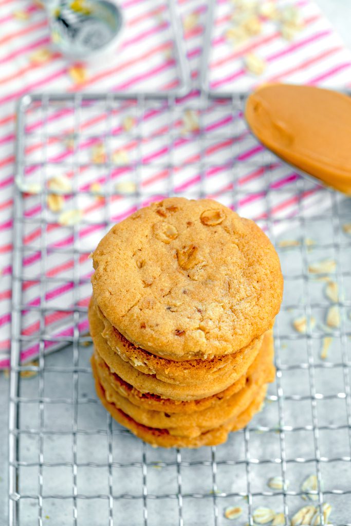 Bird's eye view of peanut butter sandwich cookies stacked on top of each other on cooling rack with spoon full of peanut butter and oats scattered everywhere