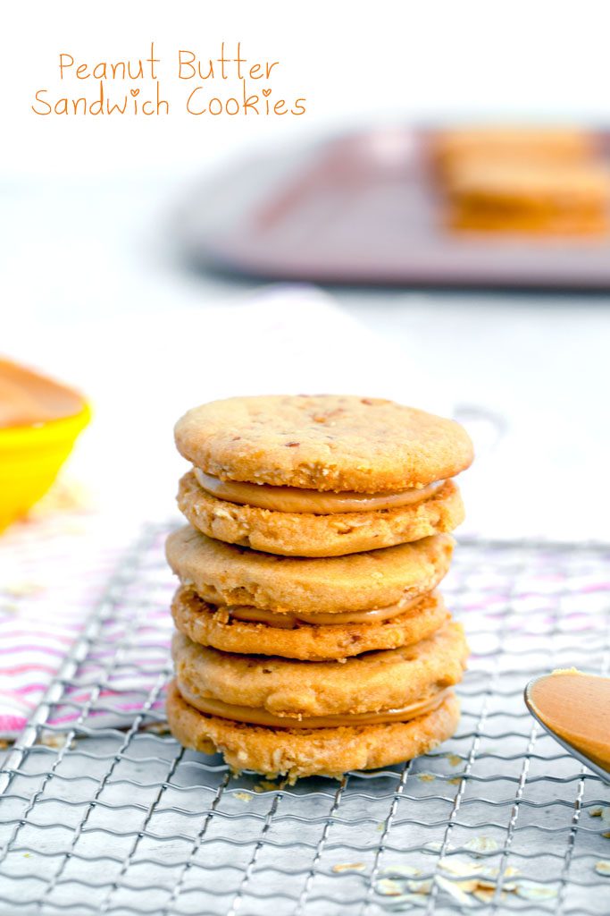 Head-on view of a stack of three peanut butter sandwich cookies on a cooling rack with spoon of peanut butter and cookies in the background with recipe title at top