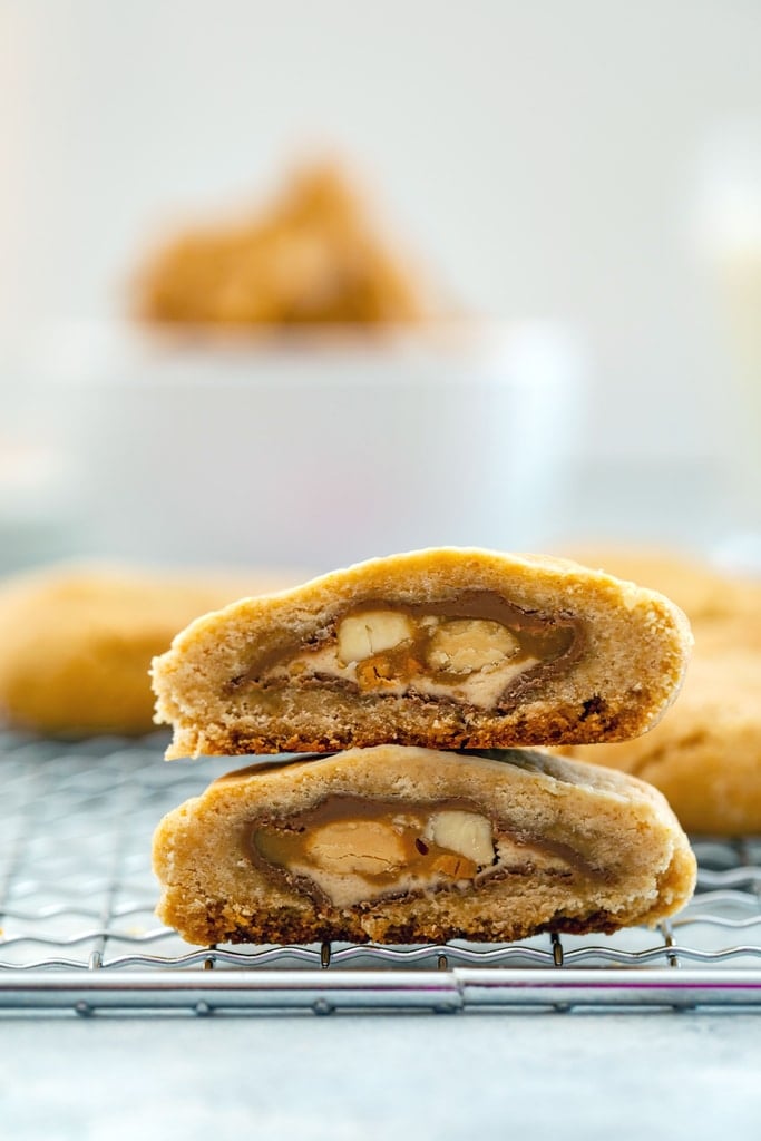 Head-on close-up view of peanut butter cookie cut in half to show Snickers bar middle.