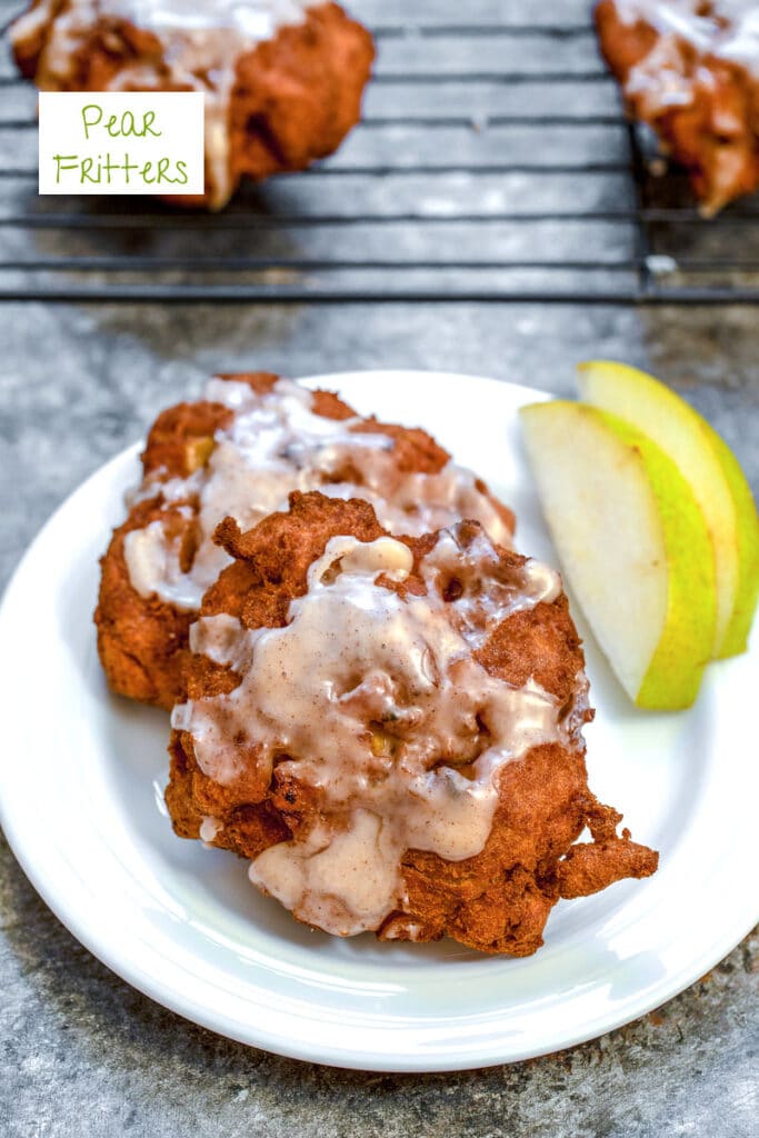 Overhead view of a pear fritter on a white plate with sliced pears, a baking rack with more pear fritters in the background, and recipe title at top