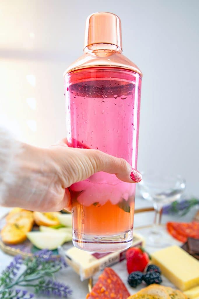 Head-on view of a pink cocktail shaker being held over a cheeseboard 