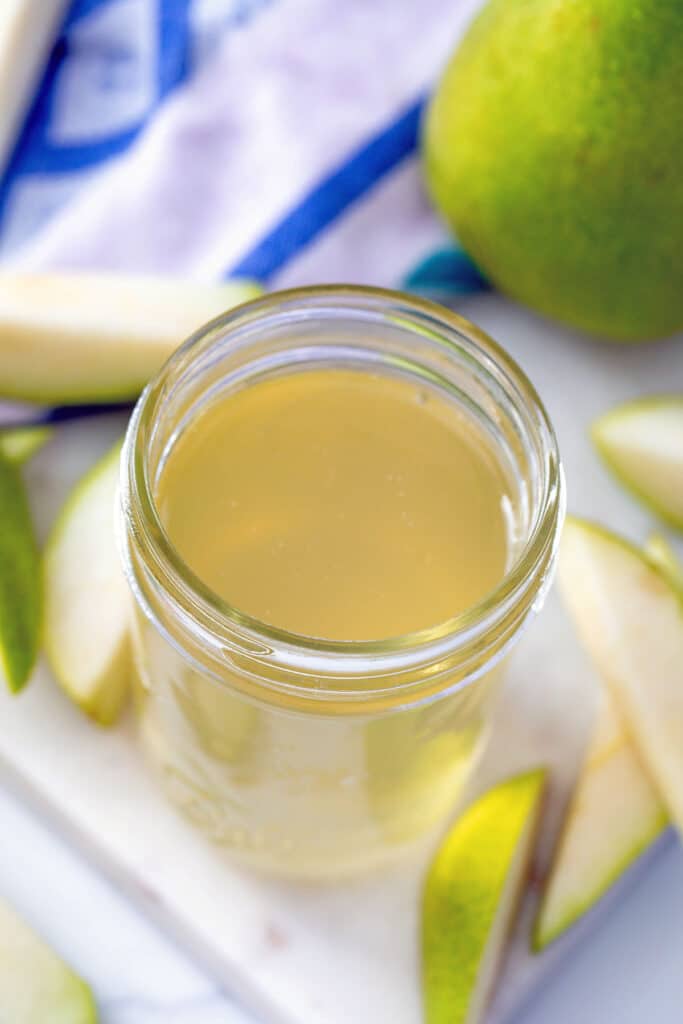 Overhead view of pear syrup in a small mason jar with sliced pears all around and a whole pear in background.