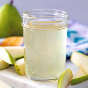 Head-on view of a small mason jar of pear simple syrup with sliced pears and a while pear in the background