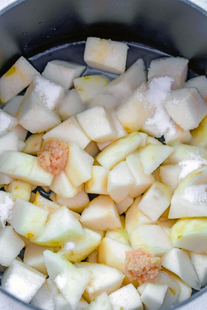 View of chopped pears in a large saucepan with water, ground ginger, and sugar.