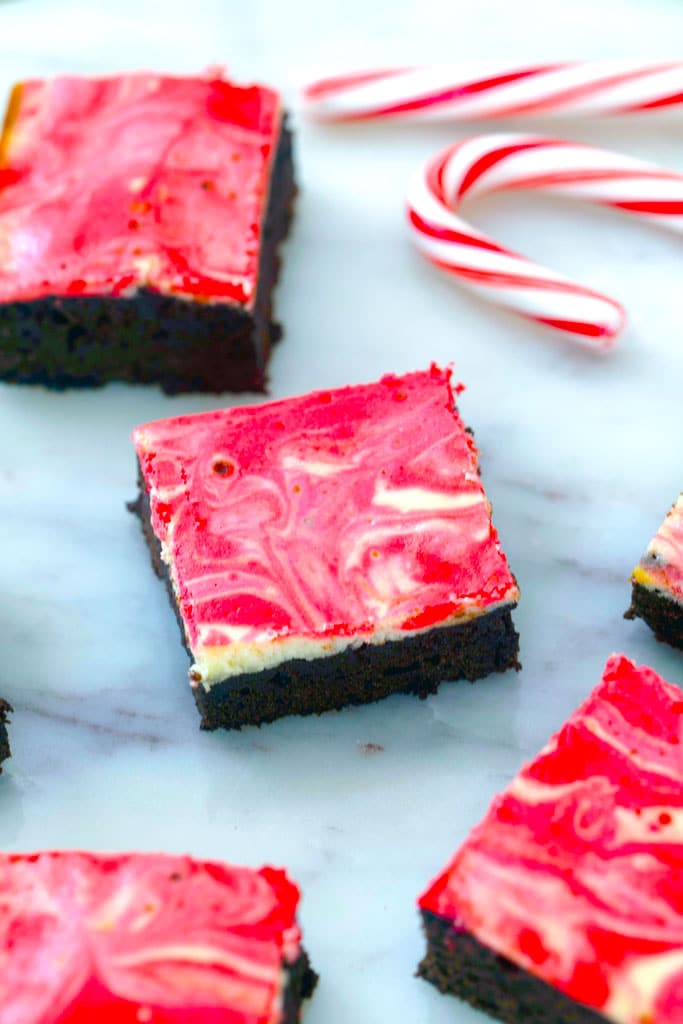Red and white swirled peppermint cheesecake brownies on a marble surface with candy canes.