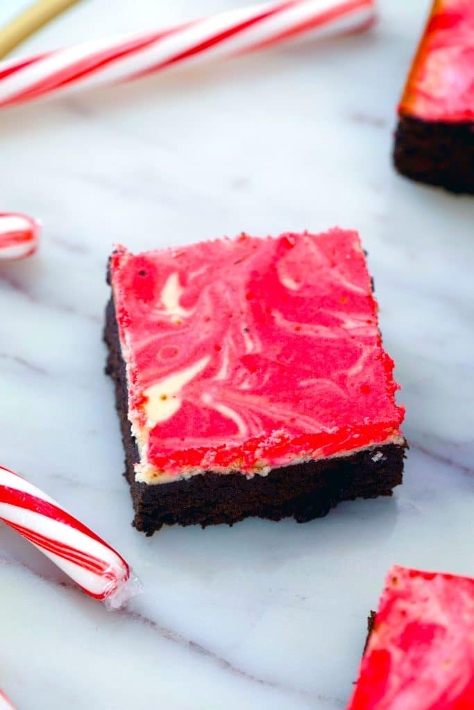 Overhead view of peppermint cheesecake brownie on a marble surface with candy canes in the background