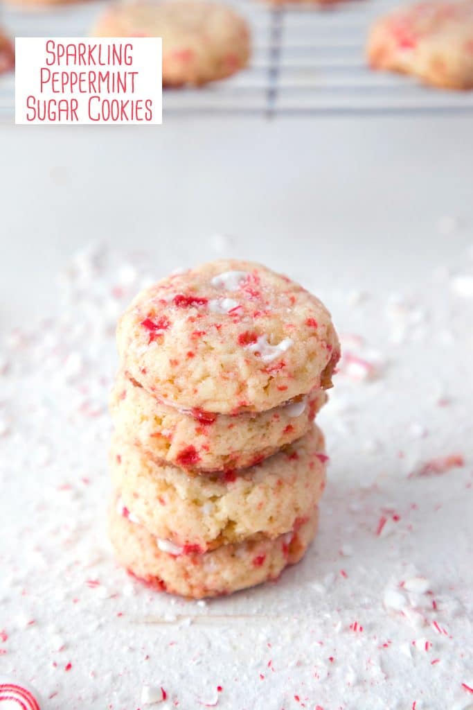 Stack of four peppermint sugar cookies on a white surface surrounded by crushed candy canes with a cookie rack and more cookies in the background and recipe title at the top of the photo