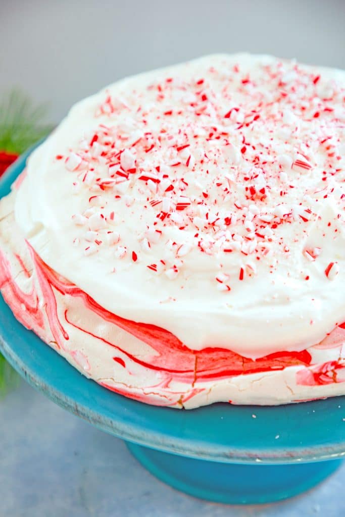 Finished peppermint white chocolate pavlova on cake platter topped with white chocolate whipped cream and crushed candy canes