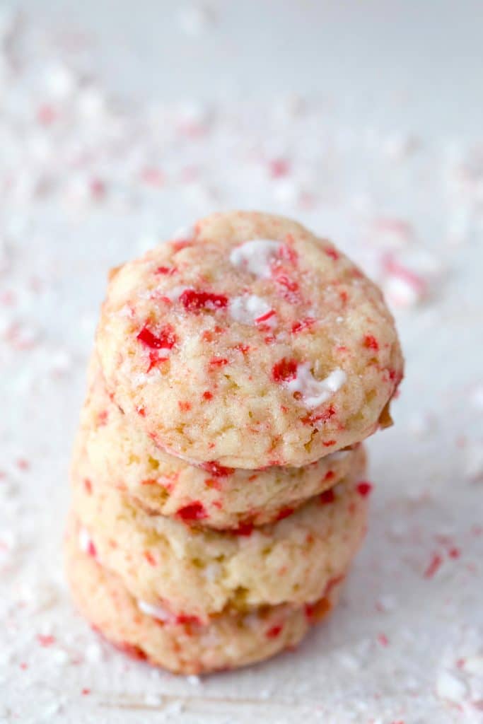 Close-up of four sparkling peppermint sugar cookies on a white surface surrounded by crushed candy canes