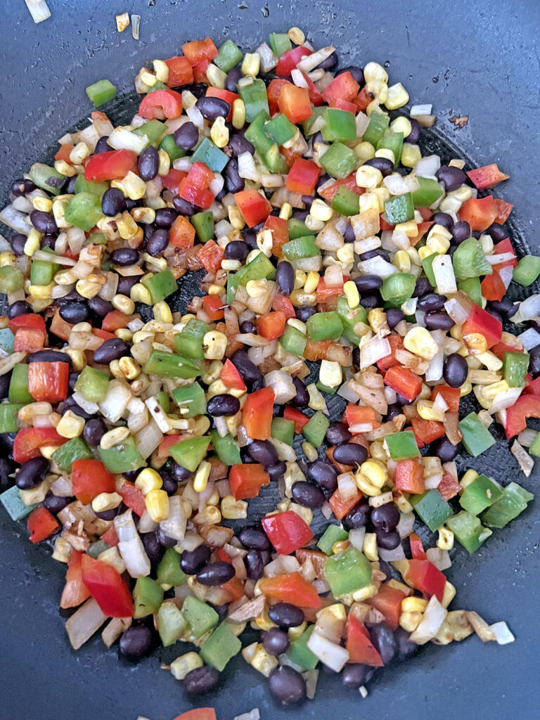 Red and green bell peppers, black beans, corn, and onion cooking in skillet.