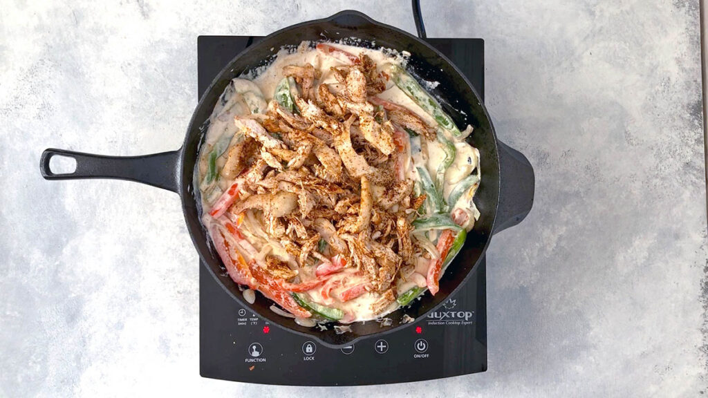Shredded chicken in skillet with peppers, onions, and creamy sour cream sauce.