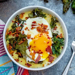Overhead closeup view of a bowl of pesto polenta topped with kale, bacon, and a runny egg