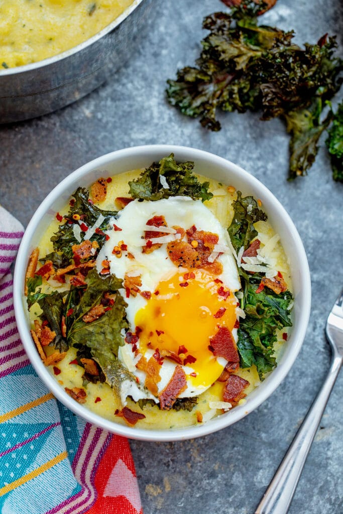 Overhead view of a bowl of pesto polenta topped with kale, bacon, and a runny egg 
