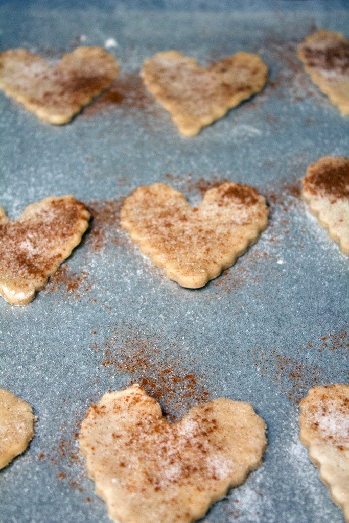 Heart-shaped pie crust cookies sprinkles with cinnamon and sugar on a baking pan ready to be baked