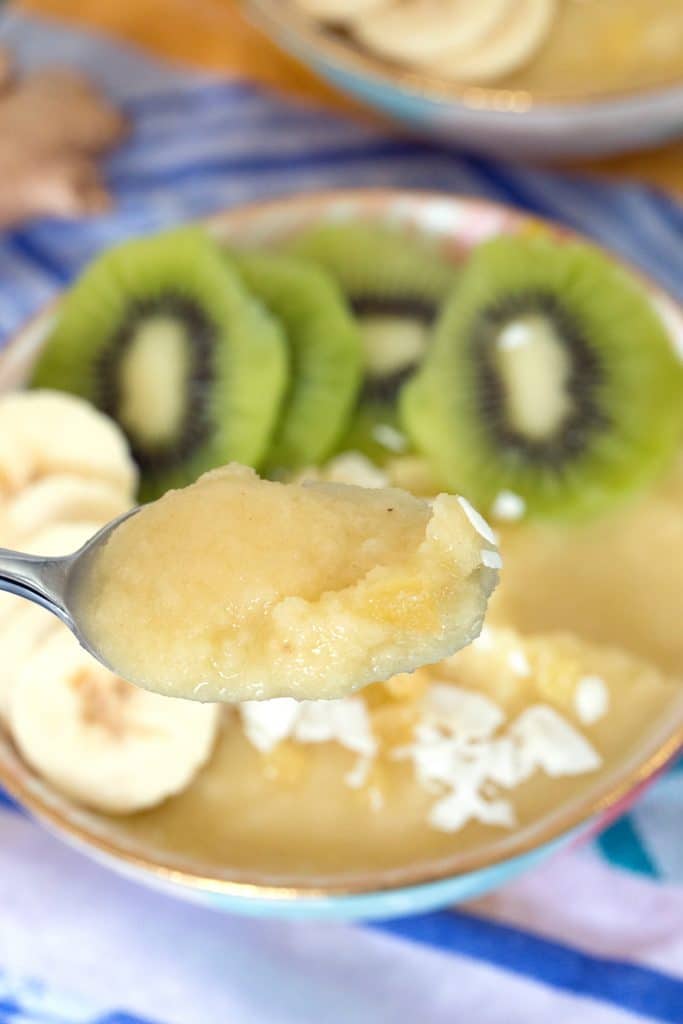 Overhead view of a pineapple banana ginger smoothie bowl with a spoonful of smoothie being held up