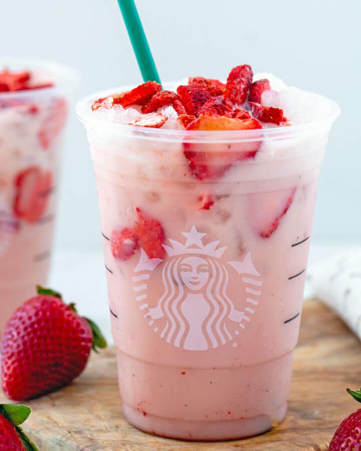 Closeup view of a Pink Drink with freeze-dried strawberries in it, fresh strawberries around, and second drink in background.