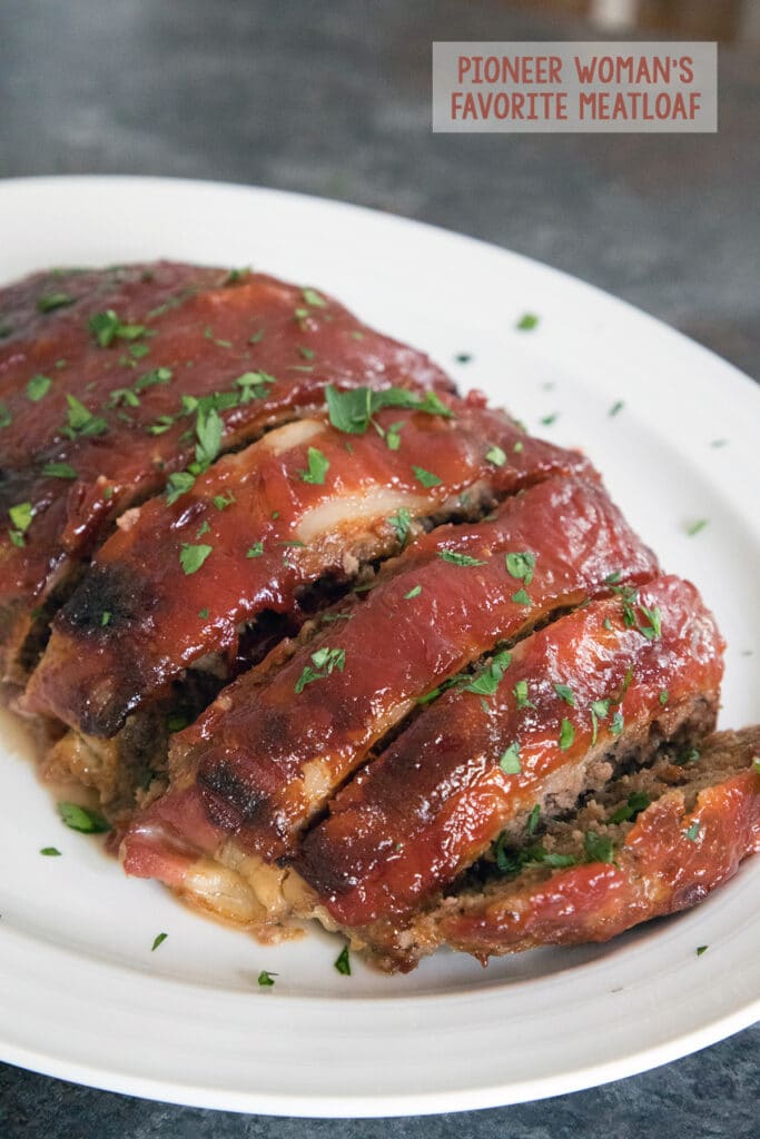 Bacon Meatloaf from the Pioneer Woman sliced on a white platter and covered in sauce and parsley with the recipe title at the top.