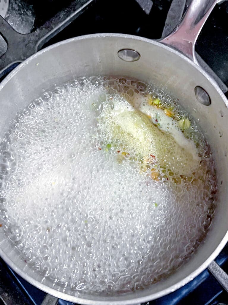 Pistachios simmering in sugar water in saucepan.