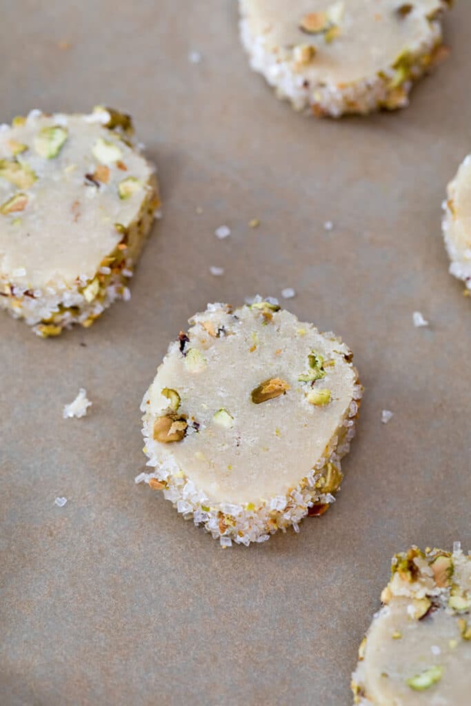 Bird's eye view of sliced pistachio cookies with edges covered in decorative sugar and ready for baking