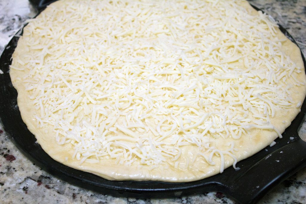 Pizza dough rolled into a round on a baking pan and covered in mozzarella cheese