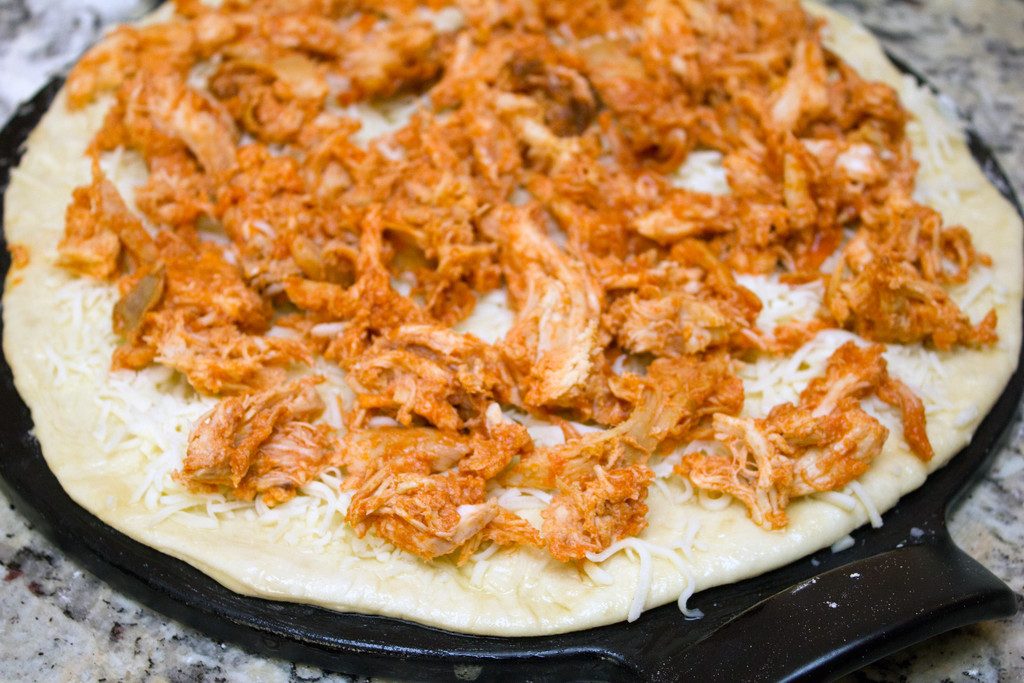 Pizza dough rolled into a round on a pizza pan and covered with mozzarella cheese and shredded buffalo chicken