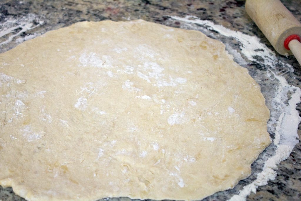 Pizza dough rolled into a circle on granite countertop with rolling pin