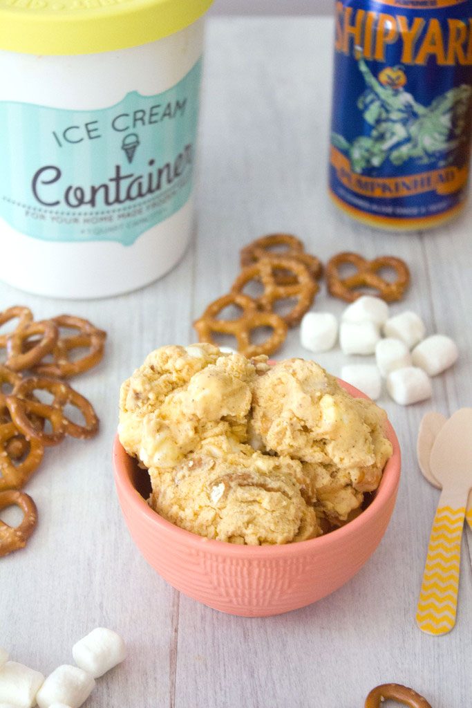 Head-on view of a bowl of pumpkin beer ice cream with pretzels, mini marshmallows, wooden spoons, can of pumpkin beer, and quart of ice cream in the background