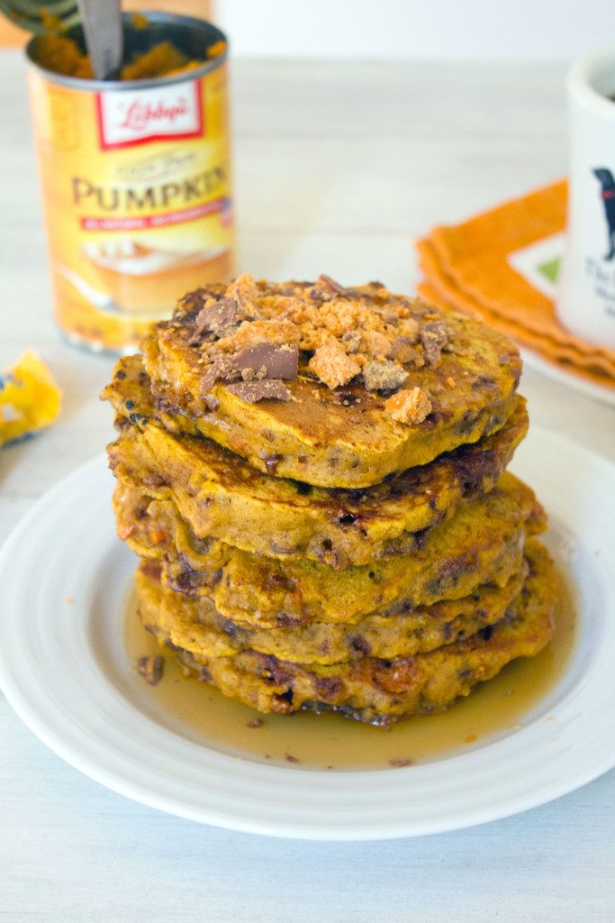 Head-on view of stack of pumpkin butterfinger pancakes with crushed Butterfinger candy on top and can of pumpkin in the background