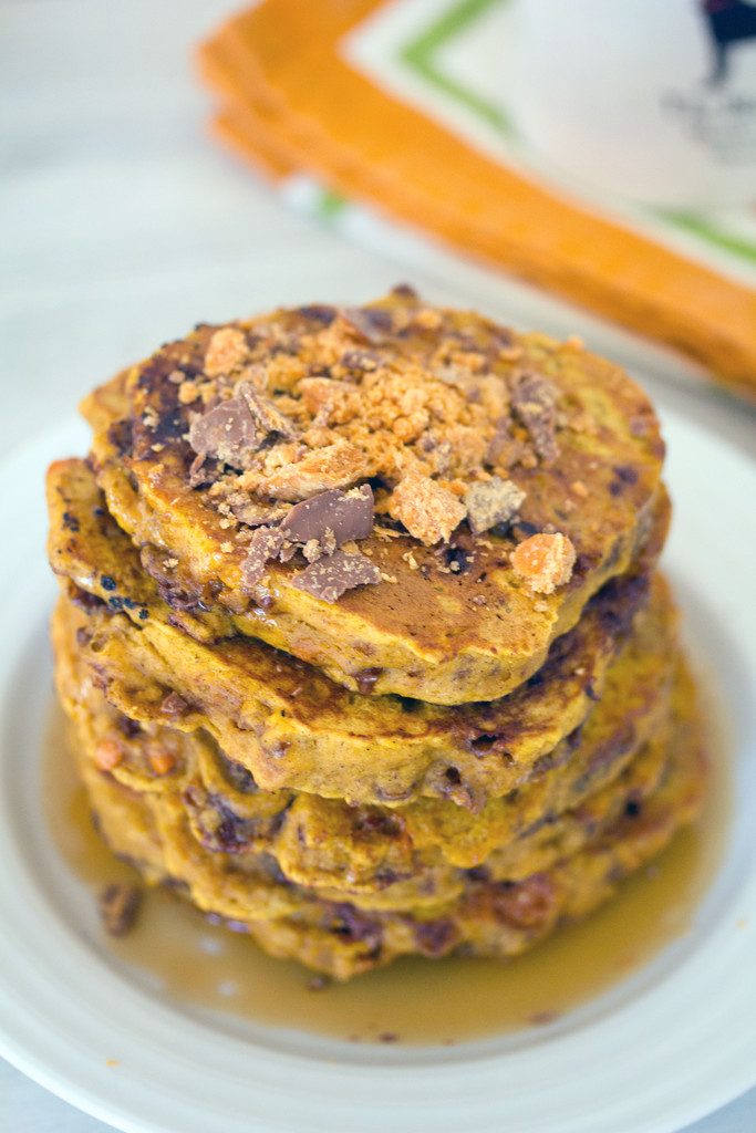 Head-on closeup view of a stack of pumpkin butterfinger pancakes with crushed Butterfingers on top