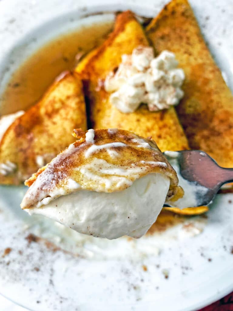 A fork with a bite of pumpkin crepe with maple cream cheese filling on it