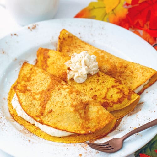 Head-on view of a plate with three pumpkin crepes filled and topped with maple cream cheese with fall leaves all around