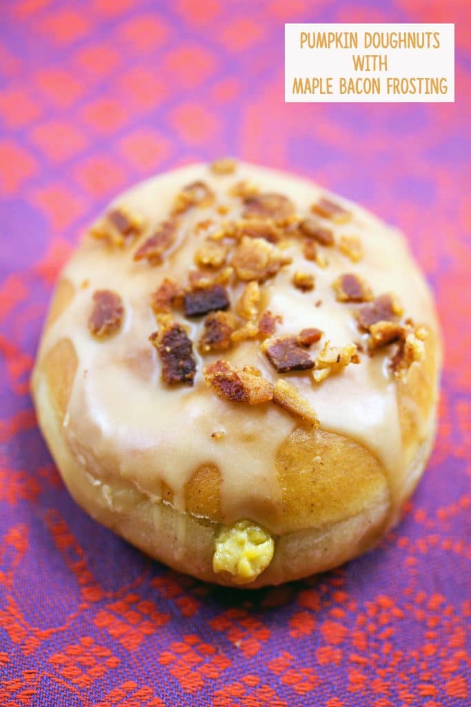 Close-up view of pumpkin doughnut with maple bacon frosting with pumpkin custard oozing out the front and crumbled bacon on top and recipe title at the top of the photo