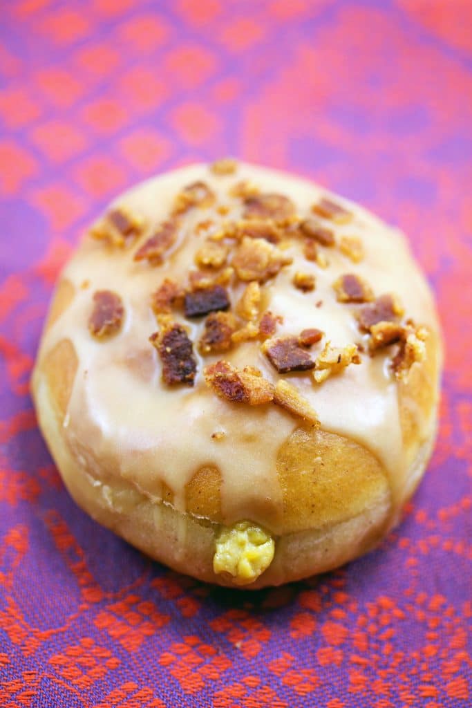 Close-up view of pumpkin doughnut with maple bacon frosting with pumpkin custard oozing out the front and crumbled bacon on top