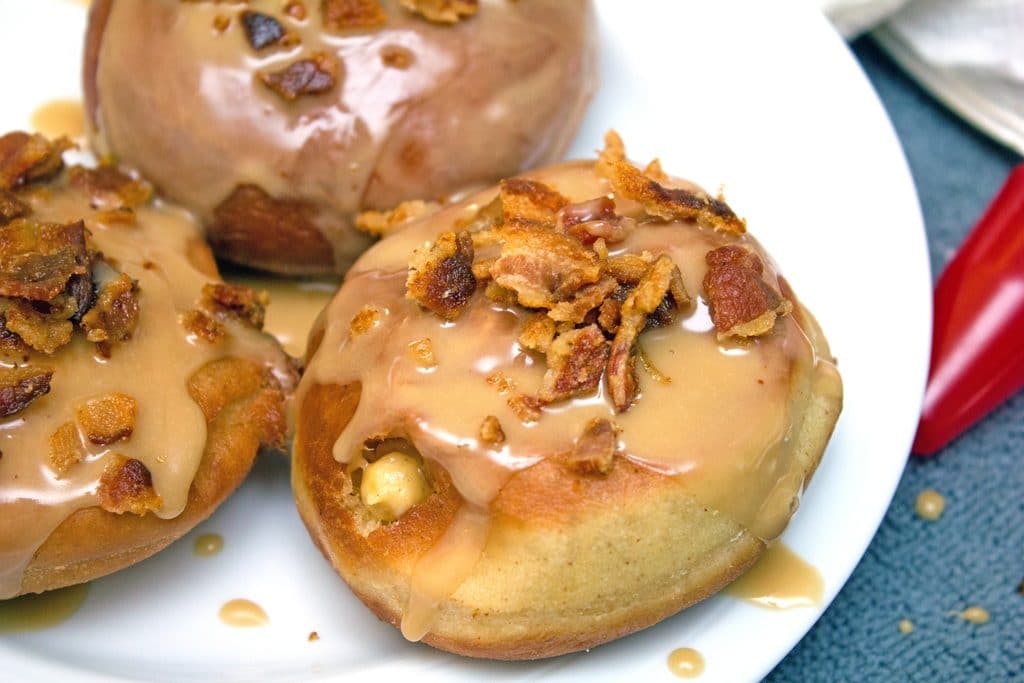 Doughnuts on a plate just filled with pumpkin custard, drizzled with maple frosting, and topped with crumbled bacon