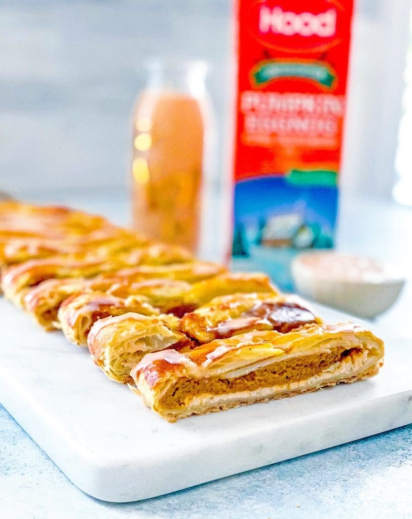 View of pumpkin eggnog danish on a marble platter with carton and glass of pumpkin eggnog and bowl of pumpkin eggnog icing in the background